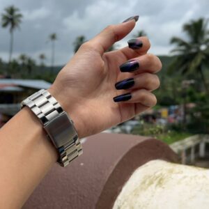 “Hand with glossy black and purple chrome nails in natural outdoor light”