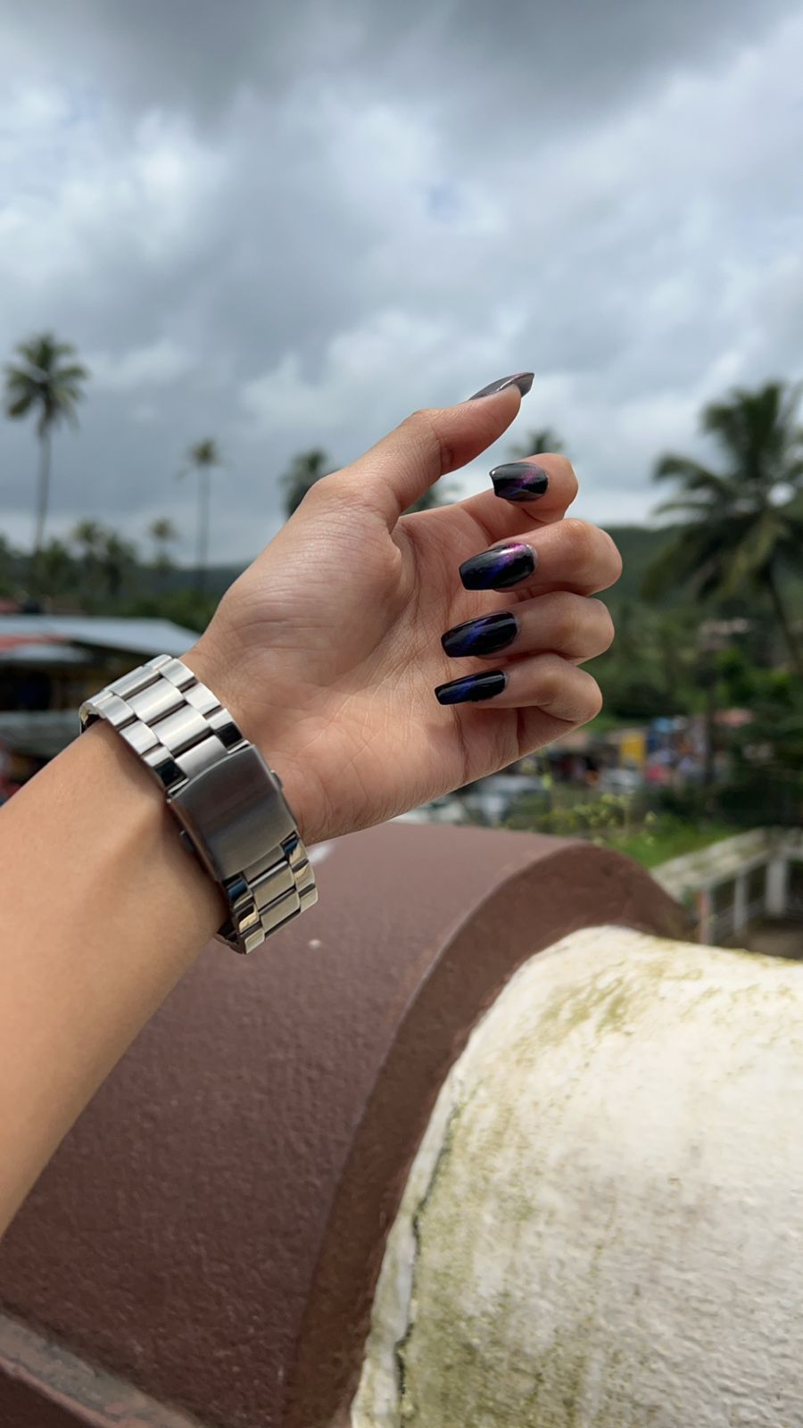 “Hand with glossy black and purple chrome nails in natural outdoor light”